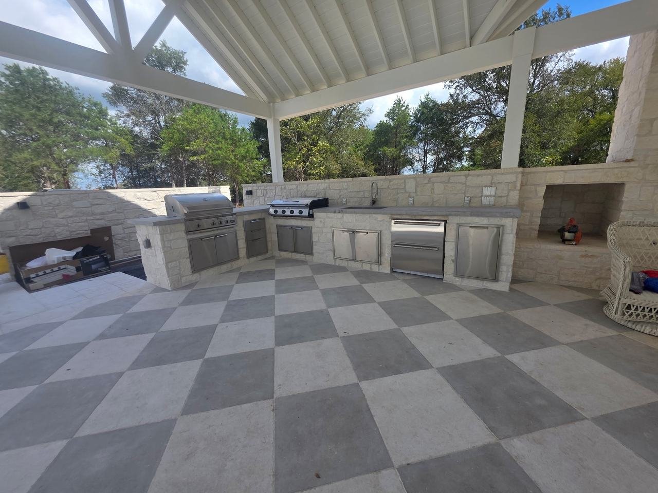 Covered outdoor kitchen with stone counters and checkerboard patio in Burton, TX