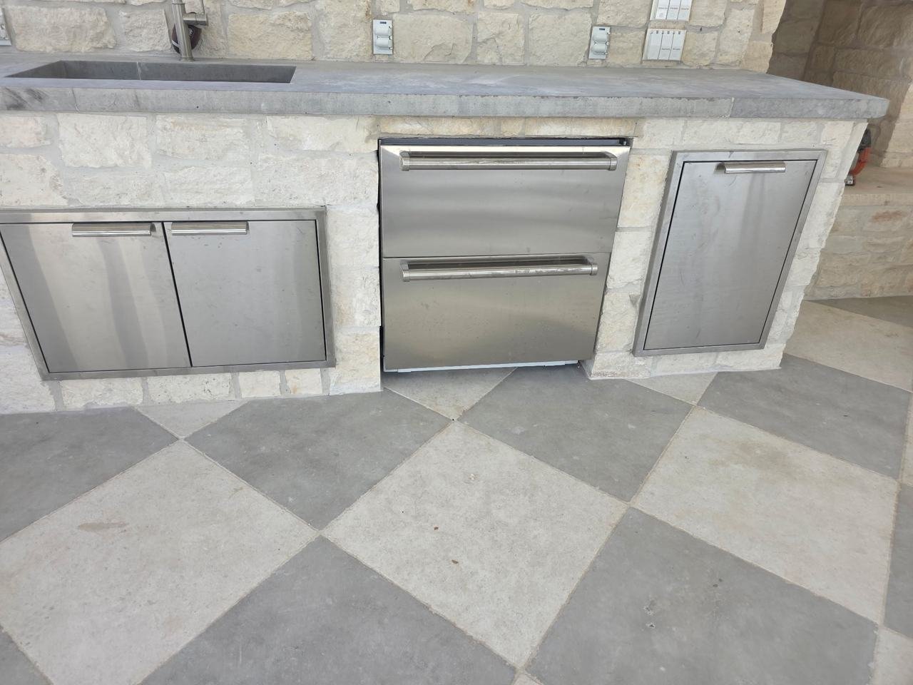 Stone-faced outdoor kitchen cabinets with stainless doors and drawers in Burton, TX